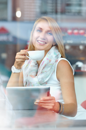 Yyoung businesswoman looking at touch pad screen while standing in modern cafe. Charming smart woman read text on her digital tablet during recreation timeの写真素材