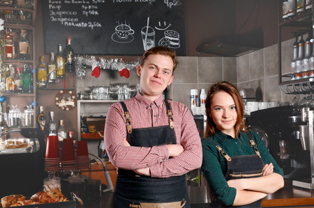 Couple of barista standing side by side in cafe. Handsome man and attractive woman are making coffee. Food and drink industry conceptの写真素材