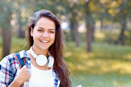 Happy student girl with backpack and headphones smile in summer park. Young woman model wearing school bag.の写真素材