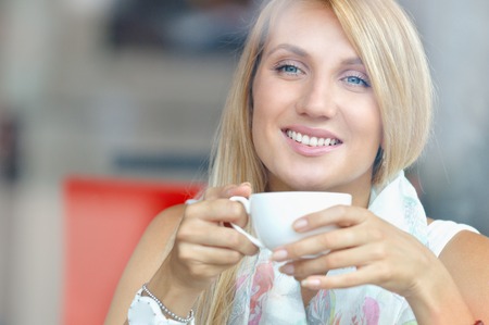 Cheerful woman with cup of coffee sitting in cafe and looking at the window. Close up portraitの写真素材