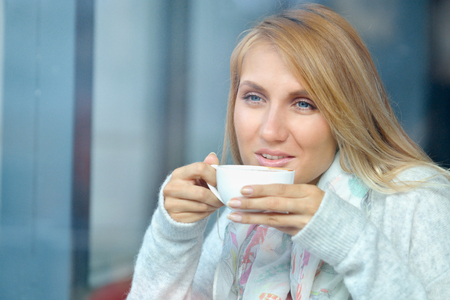 Portrait of a pensive girl drinking coffee and looking outdoors through a window. Lifestyle conceptの写真素材