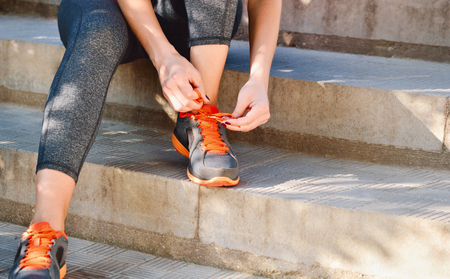 Woman tying laces of running shoes before training sitting on stairs. Outdoor lifestyle close-up of the legs of sporty young womanの写真素材