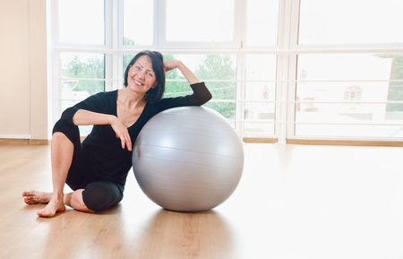Happy senior woman resting after exercise. Fit aged woman lean on the big gray exercise ball.の写真素材