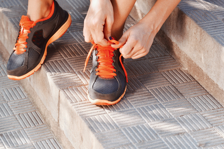 Woman tying laces of running shoes before training sitting on stairs. Outdoor lifestyle close-up of the legs of sporty young womanの写真素材