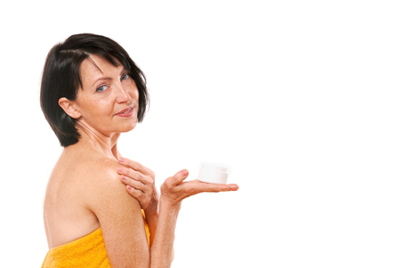 Portrait of pretty mature woman holding face cream on her hand. Isolated on white background. Beauty and care concept. Senior woman taking care about her skinの写真素材