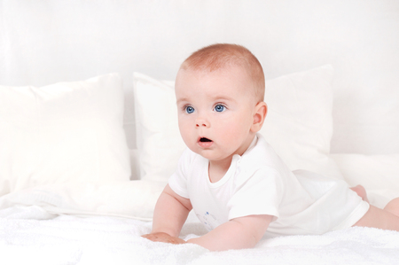 beautiful portrait of Incredible and charming small baby. Happy smiling child with blue eyes on white bed backgroundの写真素材
