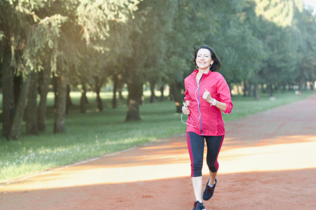 Portrait of elderly woman running in the park in early morning. Attractive looking mature woman keeping fit and healthy.の写真素材