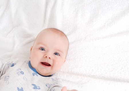 Closeup portrait of adorable newborn. Happy smiling child with blue eyes on white bed background