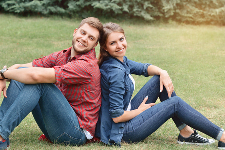 Couple siting back in back in nature. They are smiling and looking at camera.の写真素材