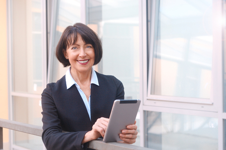 Mature businesswoman uses wireless tablet, outdoors background. Positive facial expressions. Work anywhere concept.の写真素材