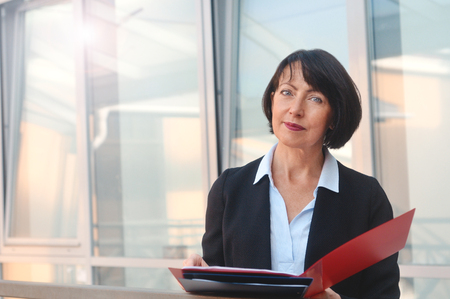 Portrait mature business woman with a folder of documents on the background of a residential building.の写真素材