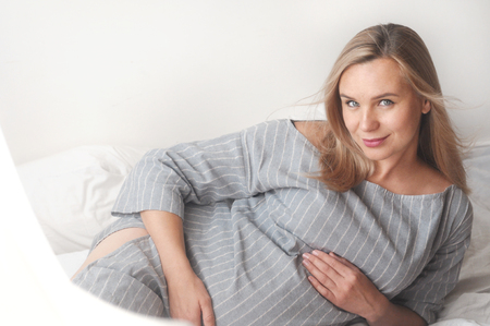 Beauty pregnant woman lie on a bed at home looking at camera. Happy motherhood conceptの写真素材