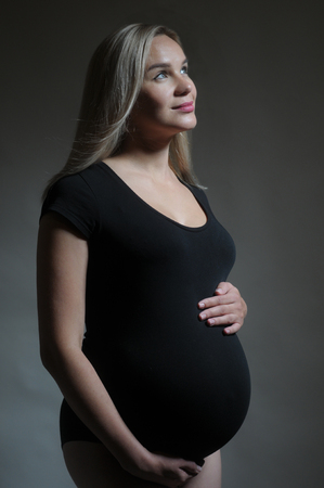 Pregnant woman holding his belly. Studio portarait on dark background. Happy motherhood conceptの写真素材