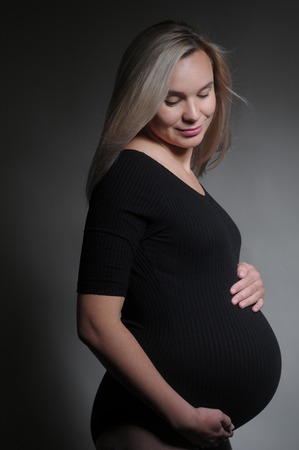 Pregnant woman holding his belly. Studio portarait on dark background. Happy motherhood conceptの写真素材