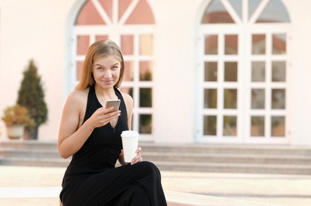 Portrait of young businesswoman using mobile phone and drinking coffee on a break at outdoorの写真素材