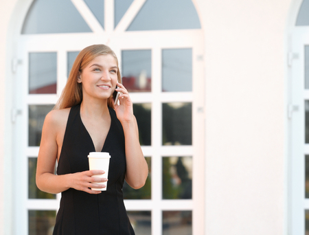 Portrait of young businesswoman using mobile phone and drinking coffee on a break at outdoorの写真素材