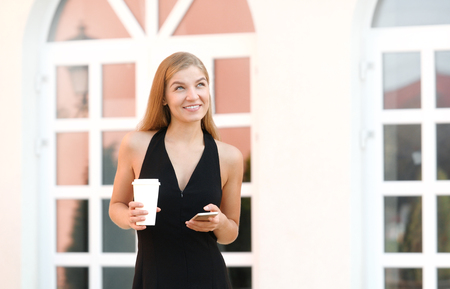 A businesswoman talking via mobile phone and holding a coffee cup against urban scene.の写真素材