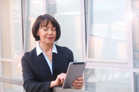 Mature businesswoman uses wireless tablet, outdoors background. Positive facial expressions. Work anywhere concept.の写真素材