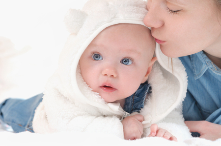 Mother play with her daughter on white bed background. Happy childhood and maternity concept.