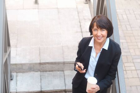 Elderly business woman with coffee using cell phone, outdoor. Work anywhere concept.の写真素材