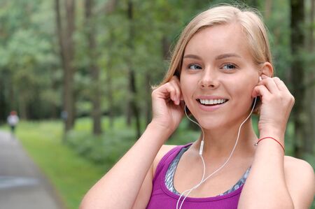 Close up portrait of young smilling sporty woman running with headphones in the fores outdoor. Healthy lifestyle conceptの写真素材