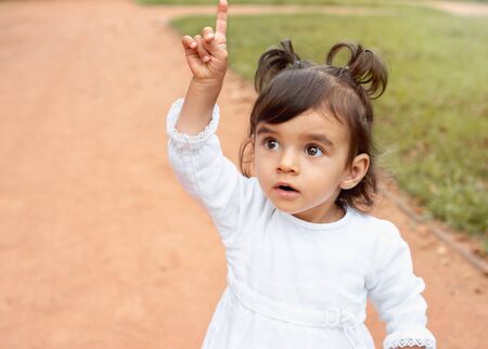 Little amazed baby girl pointing finger up in the park. Happy childhood conceptの写真素材
