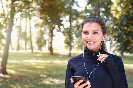 Portrait of young smilling sporty woman running with headphones in the park outdoor. Healthy lifestyle conceptの写真素材