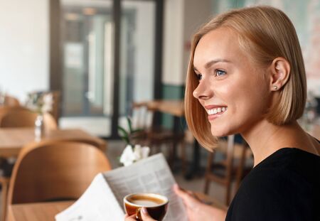 Young blonde woman having a breakfast with coffee reading newspaper in cafe. Happy lifestyle concept.の写真素材