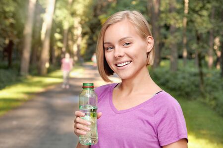 Young blonde girl drinking water during morning jogging. Healthy lifestyle concept.の写真素材