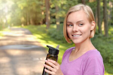 Young blonde girl drinking water during morning jogging. Healthy lifestyle concept.の写真素材