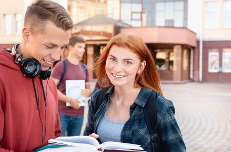 Smiling red hair teenager girl reading a classbook with her group mate against background of the university. Education conceptの写真素材