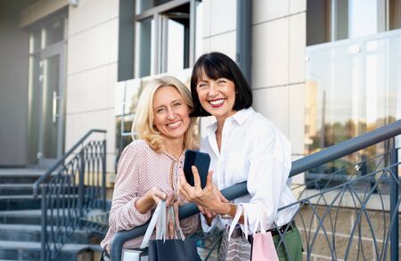 Two mature women with phone having fun while doing shopping. Pastime concept of mature peopleの写真素材