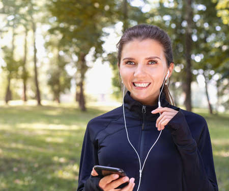 Portrait of young smilling sporty woman running with headphones in the park outdoor. Healthy lifestyle conceptの写真素材