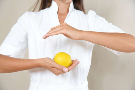 Close up photo of woman's hands in circle with lemon in a white robe. Healthy eating concept.の写真素材
