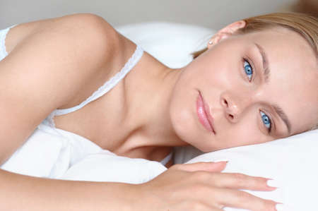 Close up portrait of beautiful young blonde woman waking up in the morning in a white bed. Self care lifestyle conceptの写真素材