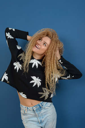 Young happy beautiful woman with blond curly hair posing on blue background. Happy lifestyle concept.の写真素材