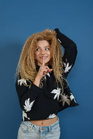 Young happy beautiful woman with blond curly hair posing on blue background. Happy lifestyle concept.の写真素材