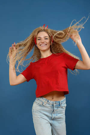 Young happy beautiful woman with blond curly hair dancing on blue background. Happy lifestyle concept.の写真素材