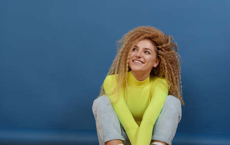 Portrait of young happy beautiful woman with blond curly hair on blue background. Happy lifestyle concept.の写真素材