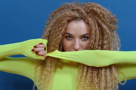 Portrait of young beautiful woman with blond curly hair on blue background. Happy lifestyle concept.の写真素材