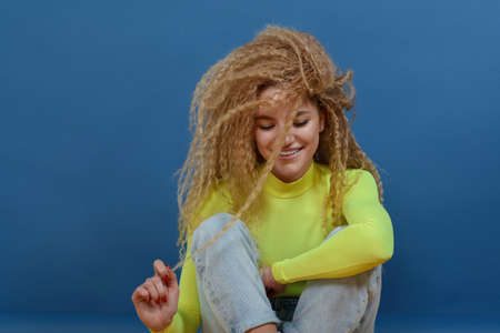 Portrait of young happy beautiful woman with blond curly hair on blue background. Happy lifestyle concept.の写真素材