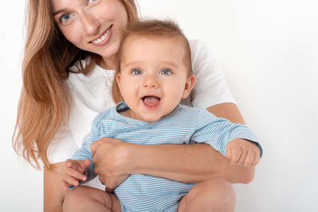 Mother holding cute happy baby boy with beautiful blue eyes on white background. Happy childhood and motherhood concept.の写真素材
