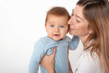 Mother holding cute happy baby boy with beautiful blue eyes on white background. Happy childhood and...