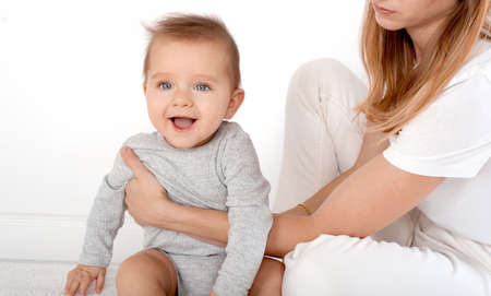 Mother holding cute happy baby boy with beautiful blue eyes on white background. Happy childhood and motherhood concept.の写真素材