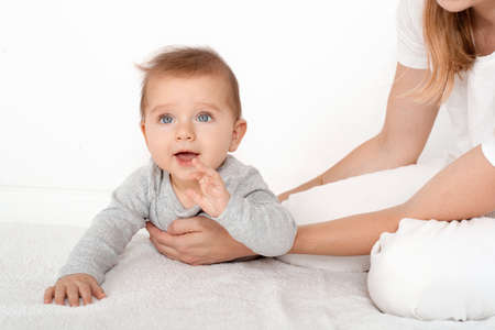 Mother holding cute happy baby boy with beautiful blue eyes on white background. Happy childhood and motherhood concept.の写真素材