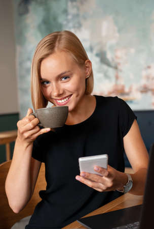 Modern business woman working on smart phone and laptop computer at coffee shop interior, internet distance work. Freelance working conceptの写真素材