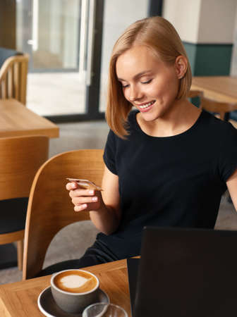 Beautiful blond woman using credit card for online payment on laptop while drinking coffee in cafe. Easy lifestyle concept.の写真素材