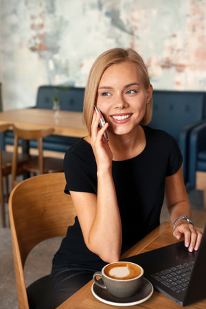 Modern business woman working on smart phone and laptop computer at coffee shop interior, internet distance work. Freelance working conceptの写真素材