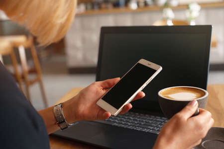 Closeup shoot of smart phone and laptop computer at coffee shop interior, internet distance work. Freelance working conceptの写真素材