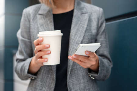 Closeup shoot of woman's hands with the phone and cup of coffee at the business center outdoors. Working lifestyle conceptの写真素材